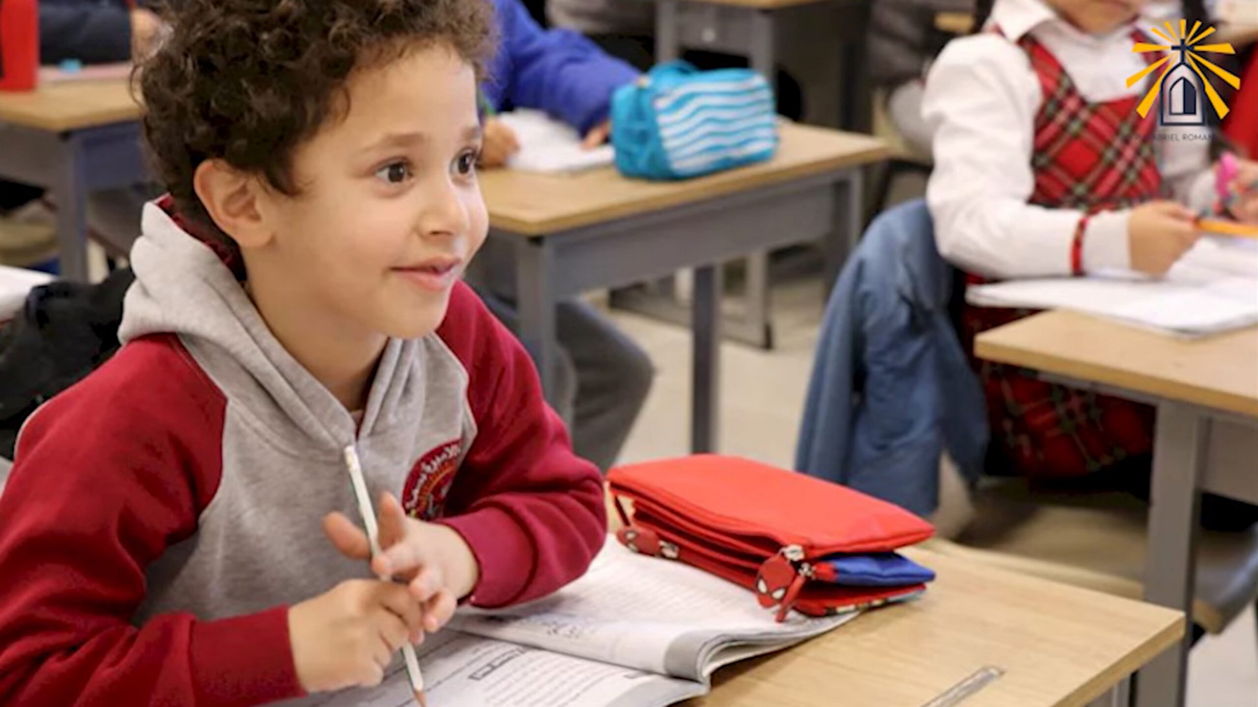 Eine Schülerin der katholischen Schule im Gazastreifen verfolgt aufmerksam dem Unterricht. Sie sitzt an einem Tisch in einem Klassenzimmer, hält einen Stift und hat ein Buch aufgeschlagen. Screenshot aus einem Video von Pater Gabriel Romanelli, dem Pfarrer der einzigen katholischen Pfarrei im Gazastreifen.