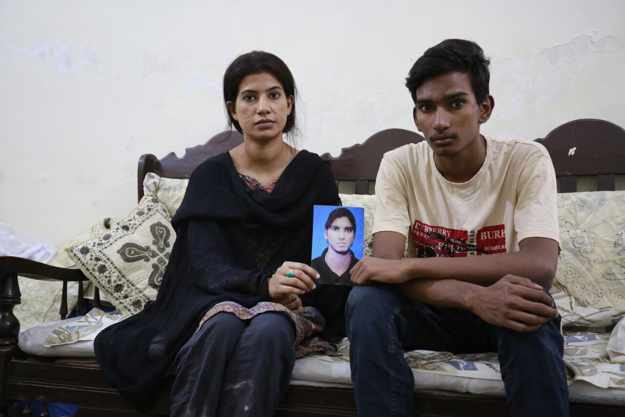 Eine junge Frau und ein junger Mann aus Pakistan sitzen auf einem Sofa und halten das Foto eines jungen Mannes in die Kamera.