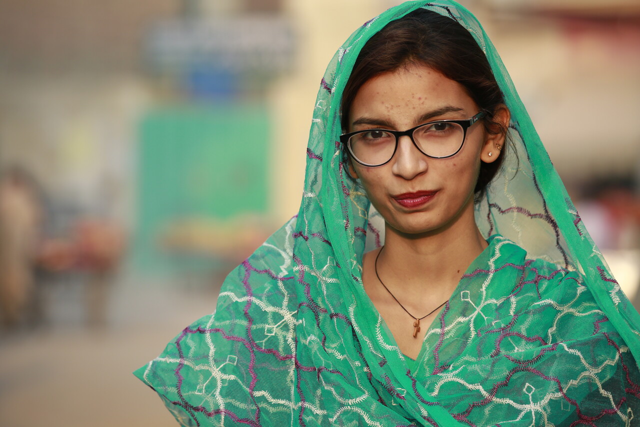 Porträt einer jungen katholischen Frau aus Pakistan mit Brille, die in die Kamera blickt.