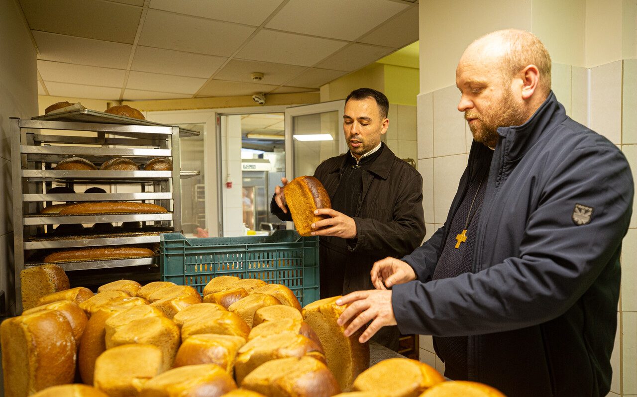 Zwei Priester begutachten frisch gebackene Brote in einer Bäckerei.
