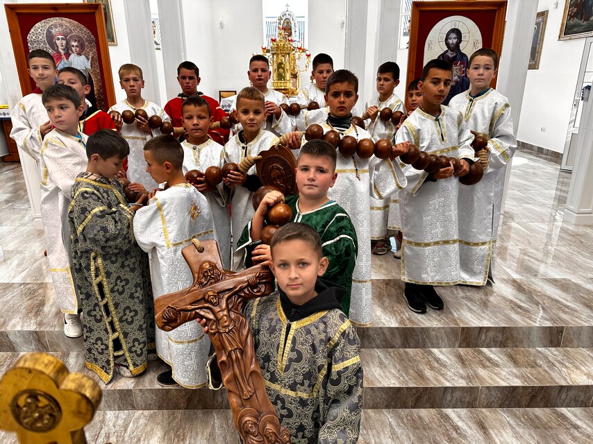 Eine Gruppe von Jungen in liturgischen Gewändern steht in einer Kirche. Mehrere halten einen großen Rosenkranz aus Holzkugeln; im Vordergrund trägt ein Junge ein geschnitztes Holzkreuz. Die Aktion Eine Million Kinder beten den Rosenkranz