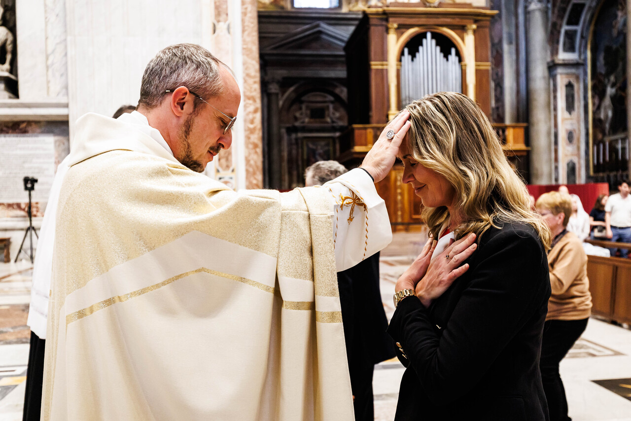 Ein katholischer Priester legt einer Frau während eines Segensgottesdienstes die Hand auf den Kopf. Die Frau steht mit geschlossenen Augen und gefalteten Händen in einer Kirche.