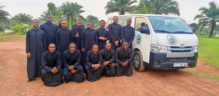 Eine Gruppe von Seminaristen posiert gemeinsam mit einem Kleinbus vor einer kirchlichen Einrichtung. Das Fahrzeug unterstützt ihre Ausbildung und pastoralen Einsätze.