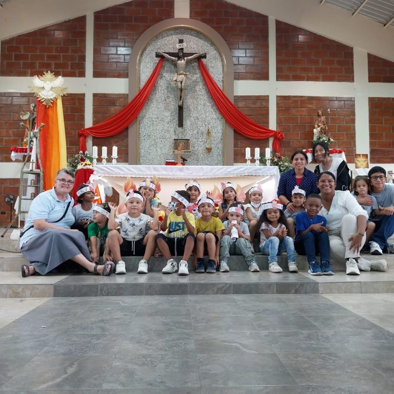 Kinder, Ordensschwestern und Betreuer posieren gemeinsam vor dem Altar einer Kirche für ein Gruppenfoto. Die Kinder tragen selbstgebastelte Kronen und lächeln in die Kamera.