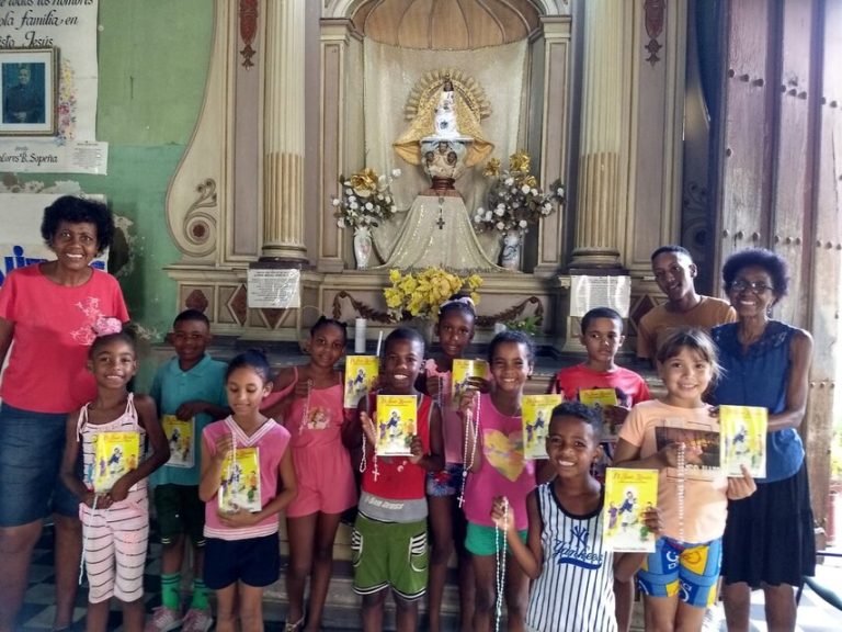 Kinder halten Kinderbibeln und Rosenkränze in den Händen und stehen gemeinsam mit Betreuerinnen vor dem Altar einer Kirche für ein Gruppenfoto.