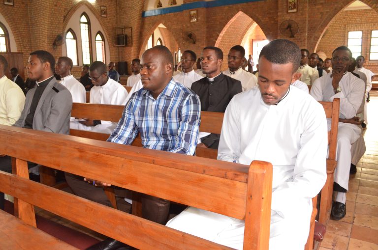 Seminaristen sitzen während eines Gottesdienstes oder einer Gebetszeit in den Kirchenbänken einer Kirche. Einige beten mit gesenktem Kopf, andere hören aufmerksam zu.